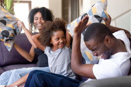 Cheerful african family sitting on sofa having fun in living room at home mom dad young parents...