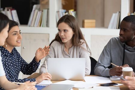 Diverse multiethnic young people sit at desk talk discuss school project consider listen to ideas,...