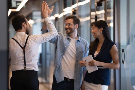 Friendly male colleagues giving high five talking standing in office hall, smiling businessmen diverse professionals group greeting meeting in company hallway work space express respect agreementの写真素材