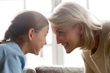 Elderly grandmother little granddaughter touching foreheads look in eyes enjoying time together...