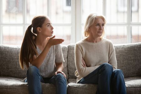 Annoyed grown up daughter expressing complaints to elderly mother annoyed females sit on couch, old stubborn mom dont want make concessions, different ages, generational gap, family conflict conceptの写真素材