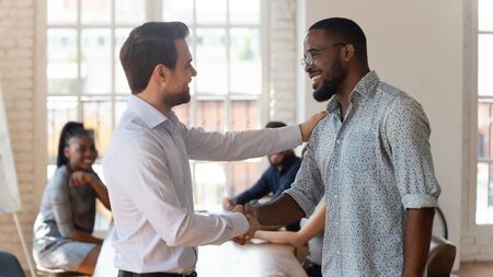 Happy black male employee get rewarded for professional achievement handshake proud white boss manager promoting supporting good african worker express acknowledgement recognition at work conceptの写真素材