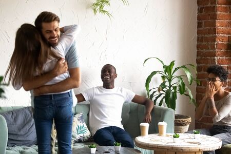 Excited millennial man and woman hug celebrating with multiracial friends in coffeeshop, young couple girl and guy embrace feel emotional and overjoyed having special celebration in cafの写真素材