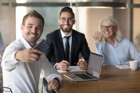 Happy colleagues employees taking selfie at workplace, young smiling businessman using phone, team, business people posing for photo at meeting in boardroom, mature businesswoman waving handの写真素材