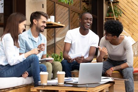 Happy multiethnic young people meet in coffee place work using laptop making notes, smiling diverse millennial friends gather in caf studying together with computer have fun laughing sharing ideasの写真素材