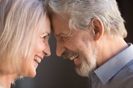 Happy old senior family couple bonding touching foreheads laughing, smiling elder husband and middle aged wife looking at each other enjoying moment of love and affection, close up faces side viewの写真素材