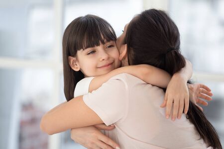 Happy cute adopted child girl hugging young affectionate mother feel tenderness connection love, smiling little kid daughter embracing mom foster parent bonding cuddling together enjoy warm momentの写真素材