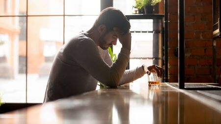 Depressed upset young man drinker addicted to alcohol drink whiskey alone in bar on daytime, sad stressed alcoholic abuse guy get drunk sit at counter with glass feel lonely desperate about addictionの写真素材