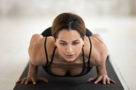 Beautiful young woman wearing black sportswear practicing yoga close up, chaturanga dandasana pose,...