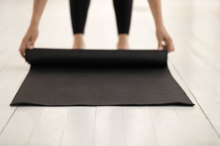 Woman rolling black mat on wooden floor close up, before or after practicing yoga at home or in yoga studio, healthy lifestyle, meditation concept, fitness, pilates equipmentの写真素材