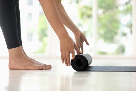 Young woman rolling black mat on wooden floor side view, feet close up, before or after practicing yoga at home or in yoga studio, healthy lifestyle, meditation, fitness equipmentの写真素材