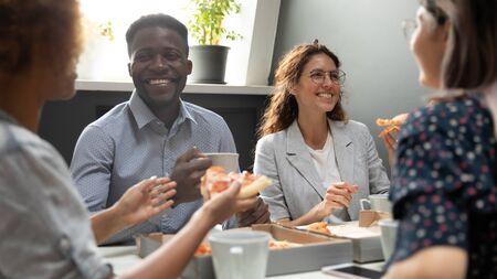 Happy african and caucasian business team people sharing pizza in office, friendly diverse...