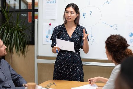 Female asian executive holding paper presenting project plan to employees group, serious vietnamese...