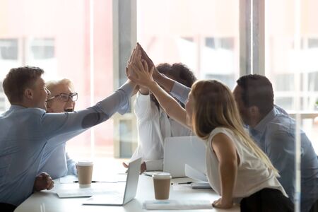 Excited multiethnic work team give high five motivated for shared success at office meeting, happy diverse colleagues join hands engaged in teambuilding activity at briefing. Teamwork conceptの写真素材