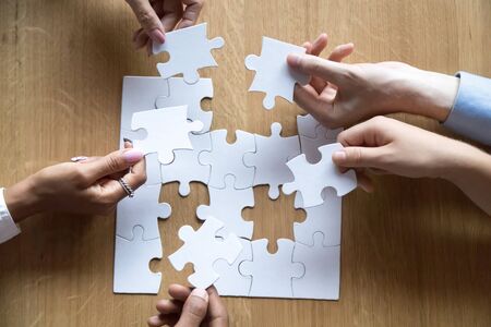 Top view of hands of diverse people assemble jigsaw helping each other looking for right decision, multiethnic businesspeople connect puzzle pieces together show unity and support. Teamwork conceptの写真素材