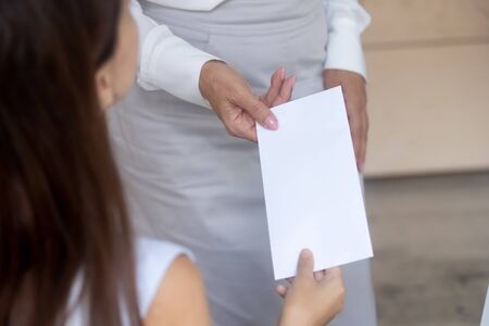 Close up of businesswoman give envelope with money reward to female worker congratulating with job success, woman boss or employer present salary bonus or extra payment to employee in officeの写真素材