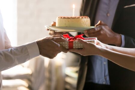 Close up employees congratulating colleague with birthday or promotion, giving gift box with bow and cake with candle, party in office, friendly workers making surprise, corporate celebration conceptの写真素材