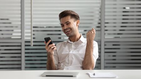 Cheerful successful motivated euphoric young manager using smartphone, received email with good...