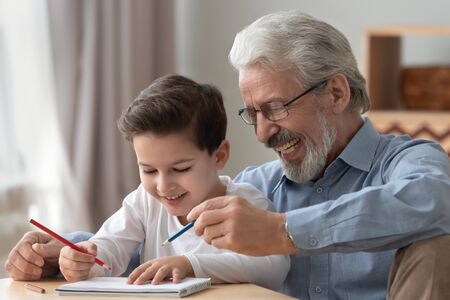 Happy two 2 generations family old grandfather helping teaching cute little boy grandson drawing with pencils together, smiling senior grandpa playing with grandchild enjoy creative children activityの写真素材