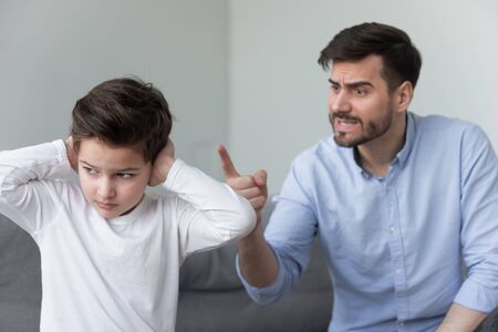 Angry mad father shouting at stubborn fussy little kid son close ears not listening ignoring dad punish rebellious kid boy for bad behavior, parents and children family conflicts arguments conceptの写真素材