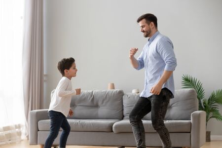 Happy active family young dad and cute little kid son dancing having fun in living room together, funny preschool small boy laughing imitating father moves, daddy child play at home leisure lifestyleの写真素材