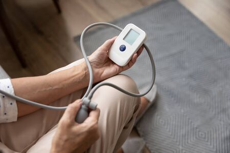 Close up mature woman checking, measuring blood pressure with digital tonometer at home, older...
