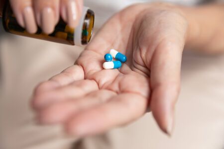 Close up mature woman taking out dose of pills from glass bottle, older female holding medicine, supplements or antibiotic, preparing to take emergency medicine, healthcare and treatment conceptの写真素材
