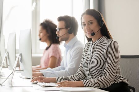 Call center workers working wearing headset use pc sitting at desk focus on young woman team member portrait, look at camera, interpersonal relations, help to client, make telemarketing calls conceptの写真素材
