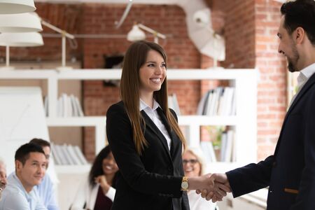 Smiling businessman handshake excited female employee congratulating with personal business success,...