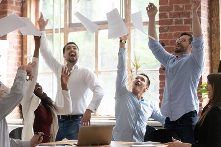 Excited diverse employees throw up in air paper documents celebrate successful business project launch, happy overjoyed multiracial colleagues coworkers feel motivated euphoric with win or successの写真素材