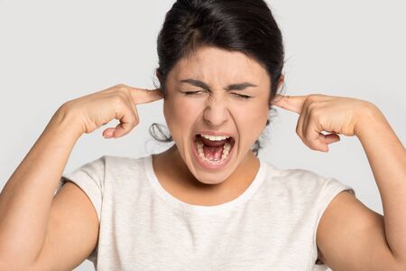 Mad ethnic young woman isolated on grey studio background close plug fingers in ears scream annoyed...