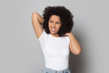 Unwell mixed race ethnicity young woman isolated on grey studio background massage back having spasm or strain, unhealthy african American millennial girl touch neck suffer from painful feelingの写真素材