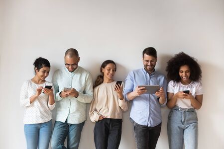 Happy diverse people using electronic devices, smartphones and tablet, standing in row on grey background, chatting in social network online, playing mobile phone games, having fun, shoppingの写真素材