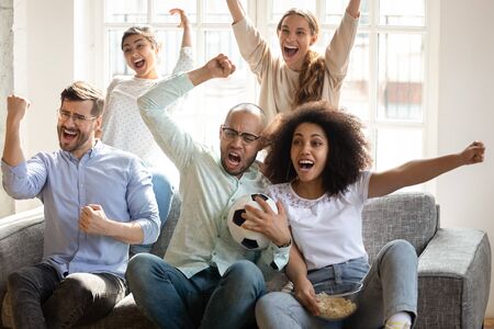 Excited diverse friends watching football match together, celebrating goal, happy fans supporting...