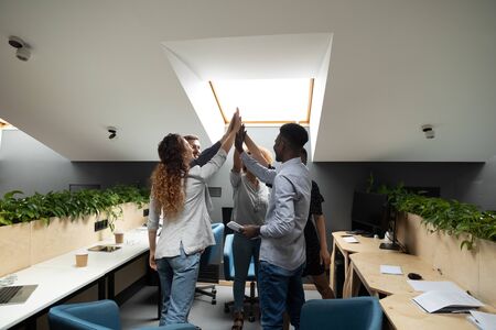 Different ethnicity millennial office workers staff members celebrating success at common business...