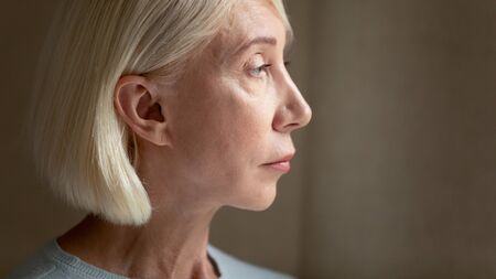 Close up head shot side view depressed elder lady looking away. Lost in thoughts upset mature woman...