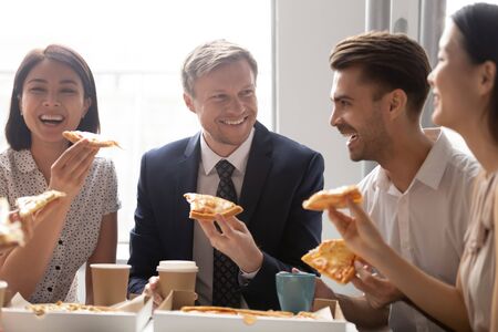 Happy diverse employees colleagues sharing meal at lunch break close up, enjoying pizza, having fun together, office workers team eating Italian fast food, laughing at funny joke, good relationsの写真素材