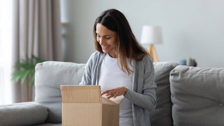 Smiling young mixed race female customer unpacking carton box, looking inside, happy get wished item...