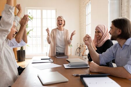 Happy older female mentor and overjoyed diverse business team people celebrate corporate triumph, staff reward together at group meeting feel motivated by victory win good work result success conceptの写真素材