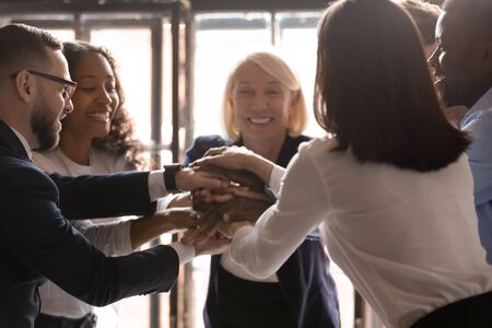 Happy united diverse business people with older mentor coach stack hands together at group meeting...
