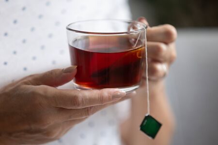 Middle aged senior woman holding cup of black bag tea, healthy mature old senior lady with relaxing...
