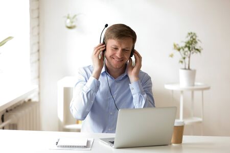Pleasant middle aged businessman wearing headphones, enjoying favorite music tracks from online...