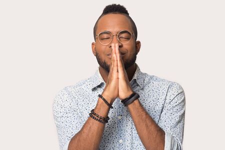 Desperate african american man in glasses isolated on grey studio background keep hands in prayer ask beg good luck, hopeful biracial male believer pray hope for best, faith, superstition conceptの写真素材