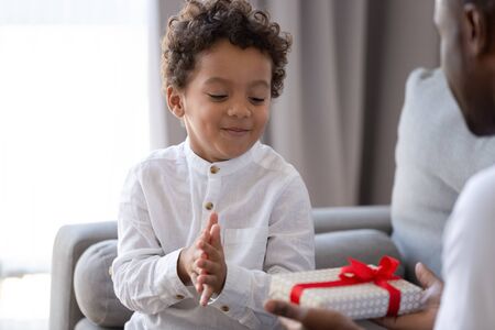 Loving african American dad hold birthday present congratulate excited little biracial son with special occasion, caring father give wrapped gift box to overjoyed small toddler child making surpriseの写真素材