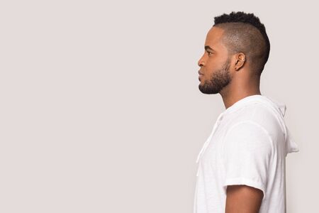 Side view of serious african American millennial man in sportswear isolated on grey studio background look straight at blank copy space, focused biracial young male in profile, free advertising spotの写真素材