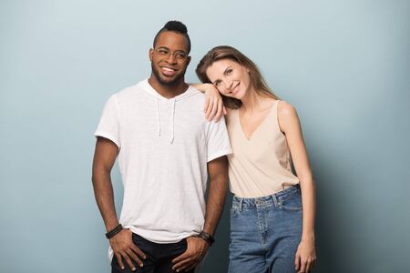Portrait of happy multiracial millennial couple isolated on blue studio background embrace posing...