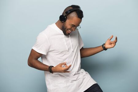 Overjoyed african American millennial man in modern earphones isolated on blue studio background have fun play imaginary guitar, excited biracial man in headphones listen to music dancingの写真素材
