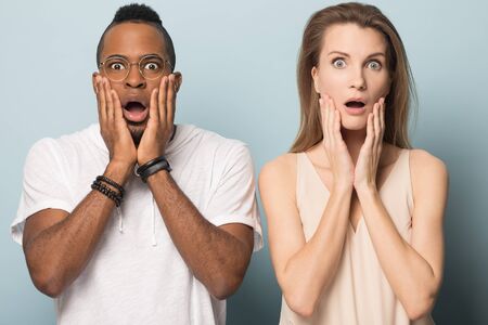 Stunned millennial multiethnic couple isolated on blue studio background round eyes jaw drop shocked by good deal or offer, surprised multiracial couple amazed by unbelievable news promotionの写真素材