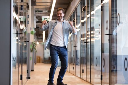 Happy smiling businessman in glasses dancing in empty modern office hallway, funny excited employee...