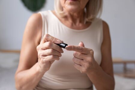 Diabetic mature woman hold use blood glucose meter in bedroom, old senior adult lady check morning insulin sugar level test with glucometer lancet on finger, diabetes diagnostic concept close up viewの写真素材